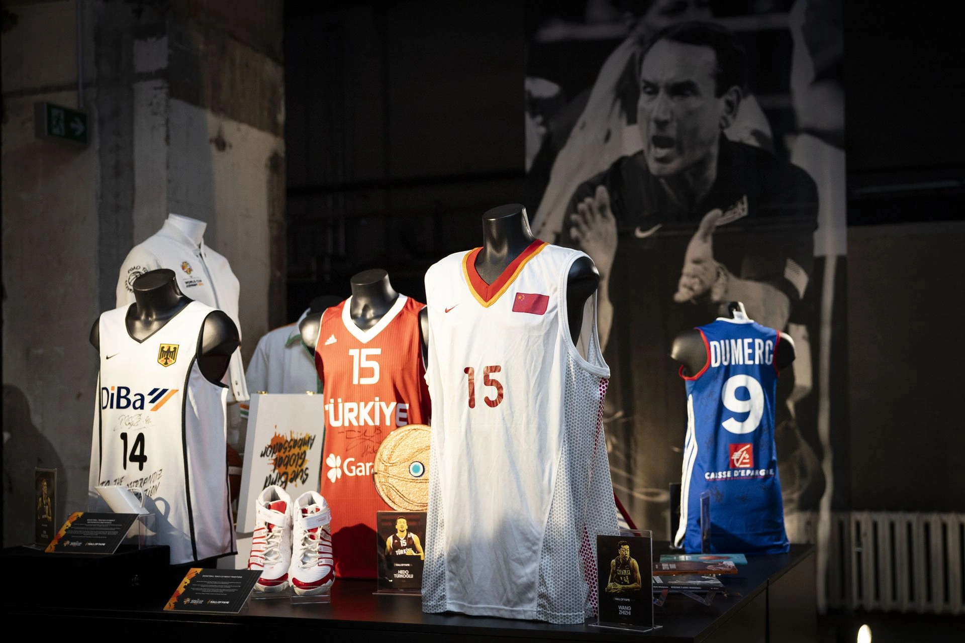 Bustes BINK Oxford FIBA Berlin Bustes Oxford noirs de BINK présentant des vestes de survêtement de basket historiques en bleu, devant un arrière-plan de photographies sportives d'époque au Kraftwerk Berlin.