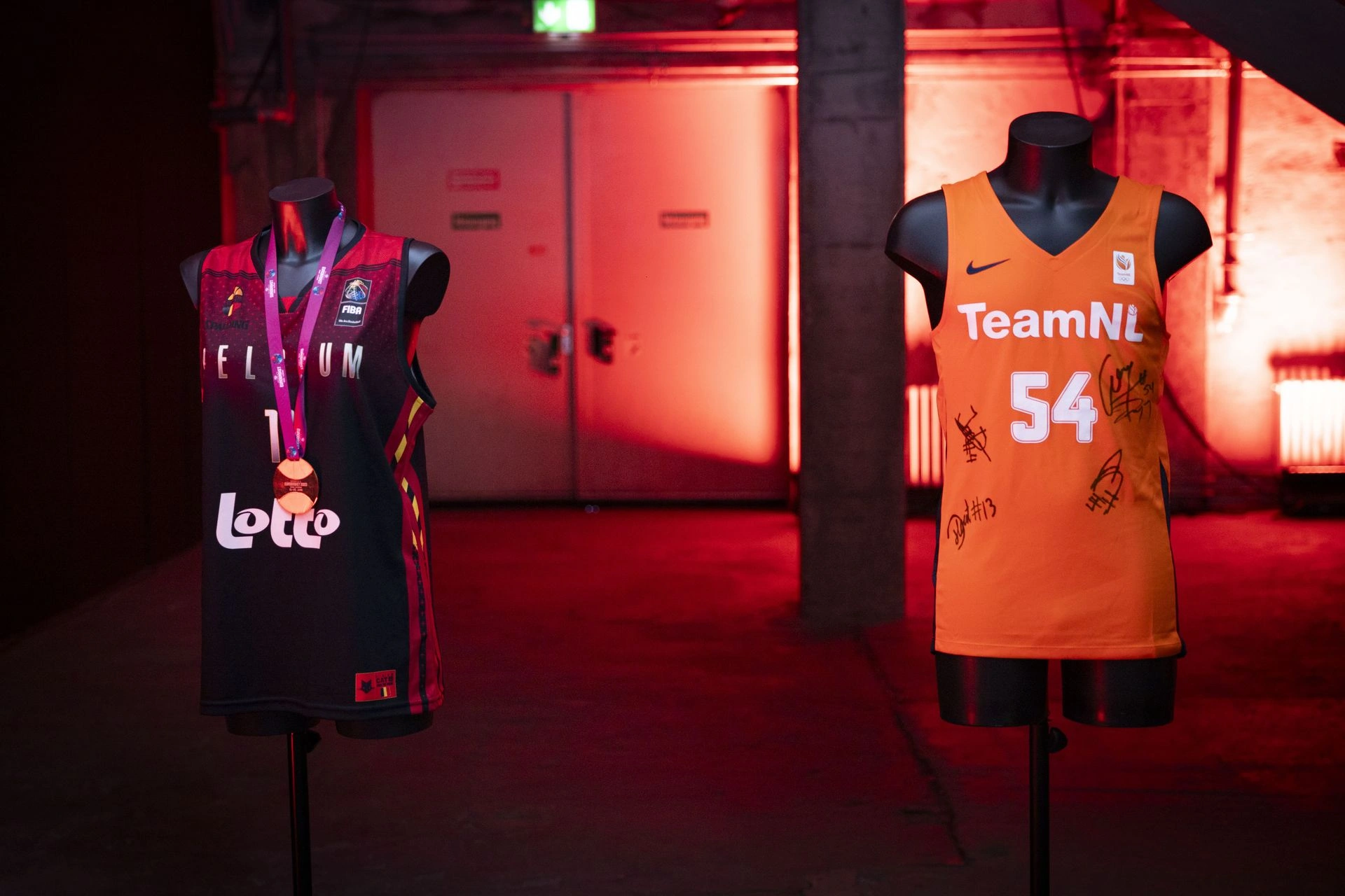 Maillots TeamNL et Belgian Cats sur bustes BINK Bustes Oxford noirs de BINK mettant en valeur le maillot orange de TeamNL et le maillot noir des Belgian Cats sous un éclairage rouge graphique au Kraftwerk Berlin.
